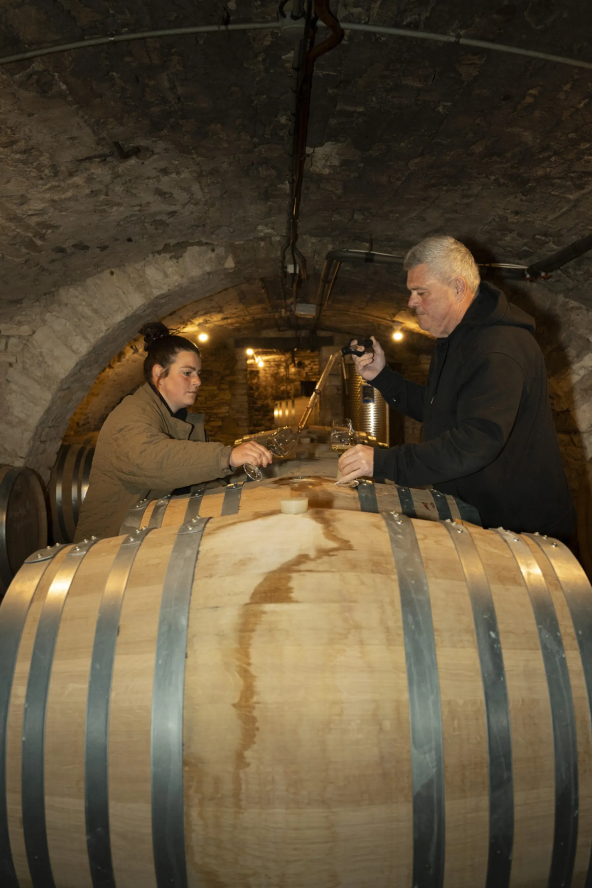 François et Jeanne Raquillet dégustant à la pipette au-dessus d’un fût, dans la cave voûtée du domaine à Mercurey